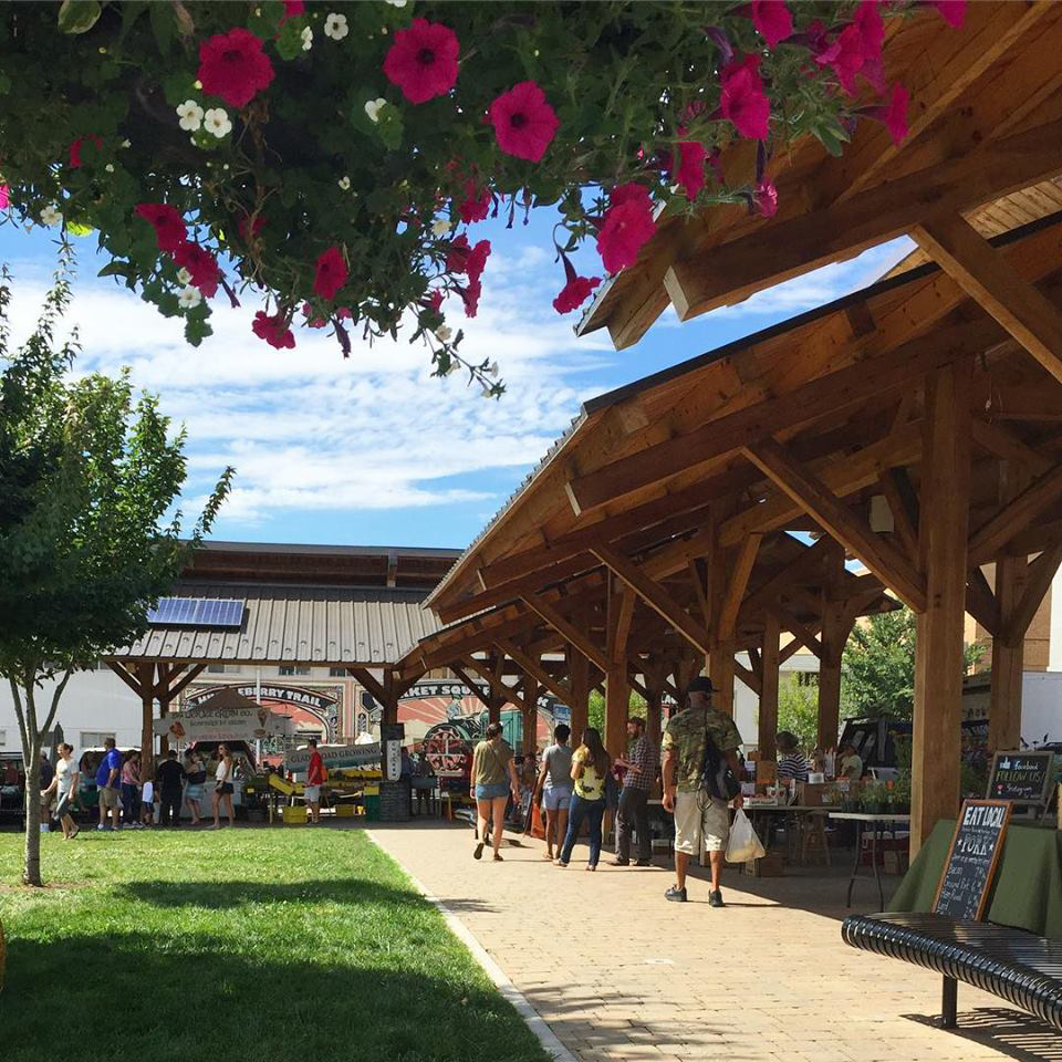 Flowers at top of image looking at Market Square Park on a Farmers Market Day with people shopping int he background